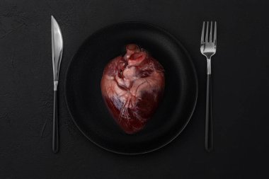 Siyah bir plaka içinde, siyah bir arka planda çatal ve bıçakla saf kırmızı bir kalp.