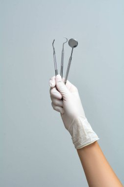 Eldiven giymiş kadın bir doktorun elinde gri bir arka planda diş aletleri bulunur..