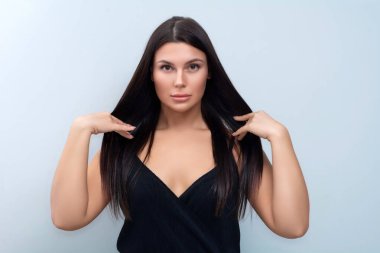 Gri arka planda siyah bir elbise içinde lüks saçlara sahip güzel bir esmerin portresi. Stüdyo fotoğrafçılık