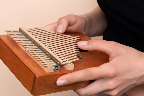 Женские руки, держащие Калимбу на бежевом фоне. Деревянный музыкальный инструмент