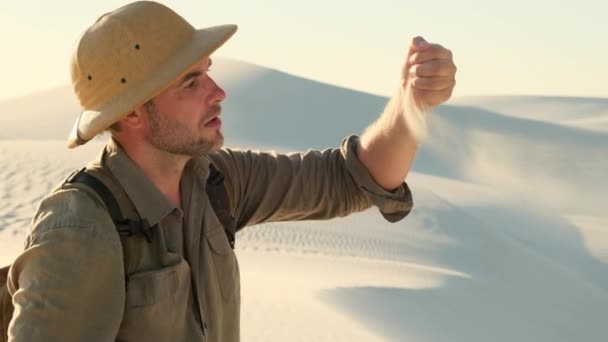 砂は人の手に渡る 国立地質公園の崖の上の旅行者 砂丘の間の砂漠で帽子を被った男が行方不明になった 砂を持つ手 — ストック動画