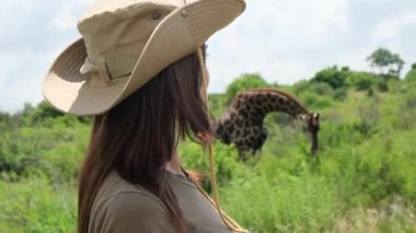 Güney Afrika 'daki Kruger Ulusal Parkı' nda zürafa. Ruaha Ulusal Parkı 'nda büyük bir zürafa. Neşeli kız gezgin Afrika savanasında güneş şapkası takmış demir bir bardaktan su içiyor. tek başına safari gezisi