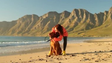 Genç bir kadın sahilde oturmuş köpeğe sarılıyor. Arkadaşlık kavramı. Kadın ve köpek kumsalda birlikte oturup güneşin doğuşunun tadını çıkarıyorlar. Plajda Golden Retriever köpeğini gezdiren yetişkin bir kadın..