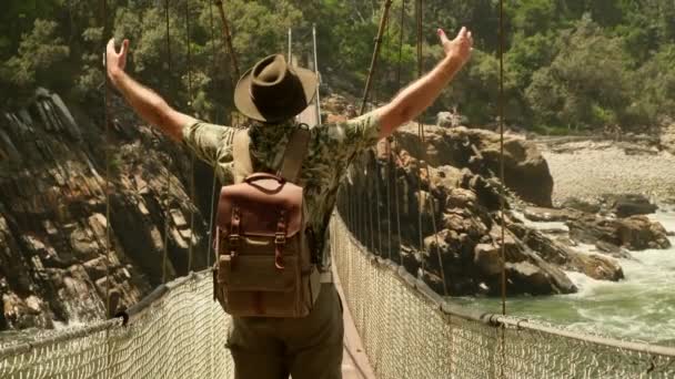 男性游客举手在靠近大海的桥上 人的绳索穿过悬在山间的桥 空中有木板的缆桥 人穿过缆桥上的缝隙 — 图库视频影像