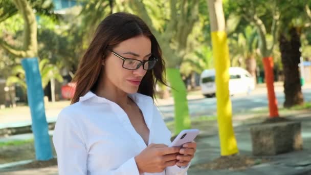 Улыбающаяся Молодая Латиноамериканка Сидящая Снаружи Городе Смотрящая Мобильный Телефон Брюнетка — стоковое видео