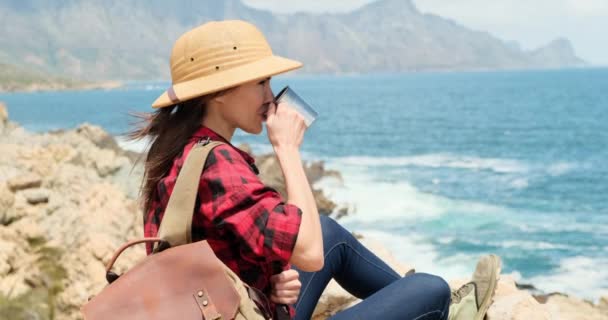 一个孤身一人在山上 一个单独旅行的女孩 一个爬山的女孩 一个坐在山上岩石上的女人 在爬山途中歇息 女游客头戴安全帽 喝铁杯里的茶 — 图库视频影像