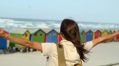 Kadın kumlu sahilde deniz dalgaları boyunca yürüyor. Güzel bir kadın deniz kıyısında sörf yapıyor. Sırt çantalı turist kız kumda yürüyor. Kadın gezgin kumsalda duruyor.