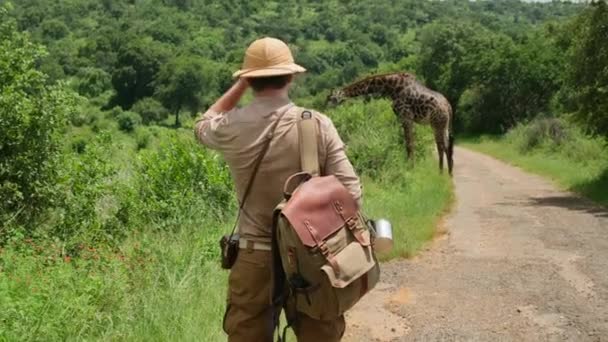 Человек Сафари Шляпе Камерой Стоит Национальном Парке Машет Жирафу Турист — стоковое видео