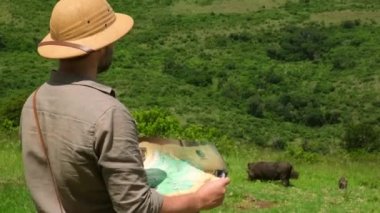 Young traveler man looking at map. Young hiker traveling and hiking alone, male using map and wearing backpack. Summer tourism, wild nature. man traveler with a backpack stands near a warthog
