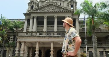 Smiling Hipster man in Glasses with Bag Walking, Looking around at Old City Street. Student, Tourist Concept. Traveling. a man in a safari hat stands near an architectural building in the city center