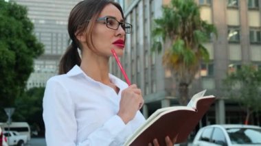female secretary in a white shirt makes an entry in the diary with a pencil. female hands holding a pen write words in a diary. Secretary writes down a task. Business woman in formal suit taking notes