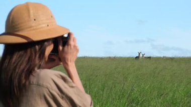 traveler in safari style photographs a animal in the savannah. Tourist On Kenya African Safari Adventure On Holiday Vacation. Wild Nature Of Search Lions And Giraffe Masai Mara. a girl in a safari hat