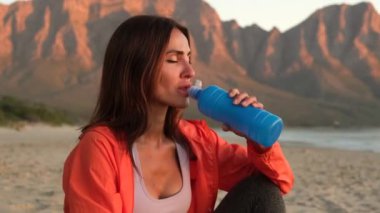 Female athlete replenishing water balance after fitness workout. Relaxed fit girl drink water from bottle. Close backlit portrait of active woman drinking from water bottle while resting from training