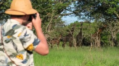 Zanzibar Afrika Safari Tatil Macerası Turisti. Vahşi Arama Zürafası. Afrika Nehri Safari Macerası Seyahati. Safari elbiseli bir erkek gezgin zürafanın yanında duruyor.