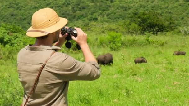 Manlig Turist Safarikläder Tittar Genom Kikaren Bakom Vildsvin Afrikansk Savann — Stockvideo