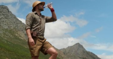 male tourist with backpack drinking fresh mountain water while a hiking. man drinks water on peak of the mountain after a long journey to the top. traveler with backpack drinking water from a bottle