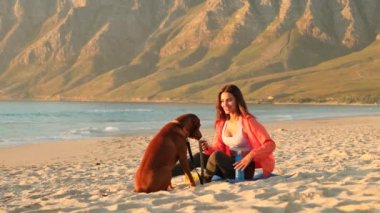 Healthy couple relax and enjoy romantic outdoor vacation together. woman and man on ocean beach playing with dog during honeymoon. man comes up and takes the girls hand and together enjoying sunrise