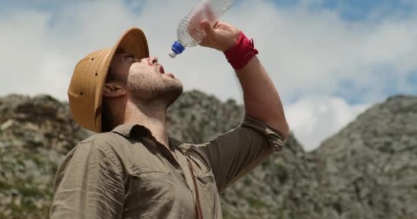 ハイキング中に新鮮な山の水を飲むリュックを持つ男性観光客 男は頂上への長い旅の後に山の頂上に水を飲む 旅行者はボトルから飲料水を飲み — ストック動画