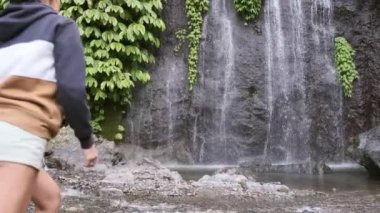 Seyahat ve özgürlük. Kadın tropikal şelale manzarasından hoşlanıyor. Endonezya, Bali 'de şelale ve kadın gezgin. Kollarını kaldırarak gururla duran bir kız. Büyük şelale duvarının önünde..
