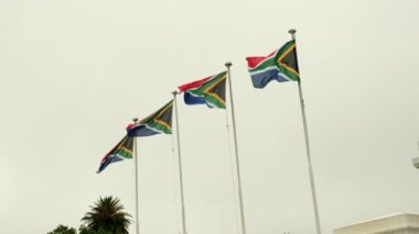 Mavi gökyüzüne karşı rüzgarda dalgalanan dört Güney Afrika bayrağı. Güney Afrika bayrağı sisli bir gökyüzüne karşı