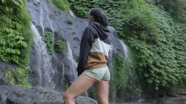 旅行和自由 正在欣赏热带瀑布美景的女人 印度尼西亚巴厘岛的瀑布和女游客 她骄傲地站在巨大瀑布前的水墙前 — 图库视频影像