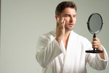 Gülümseyen adam, banyo aynasına bak. Tıraş losyonunu yüzüne sürdükten sonra sür. Erkekler için kozmetik kremi. Spa erkek modeli, cilt bakımı için cilt bakımı. Yaşlanma karşıtı cilt için sabah maskesi. Cilt bakımı.