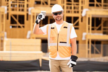 Kahve, mühendis ve inşaat işçisi şantiyede dinleniyor. Kameraya gülümseyen kasklı yakışıklı erkek müteahhit. Görevli inşaat işçisi. Müteahhit ve Tahta Ev Çerçevesi