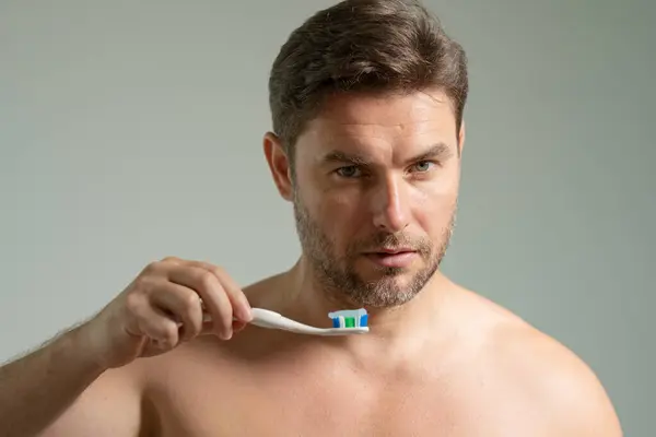 Man applying toothpaste on brush in bathroom, closeup. Attractive man looking down on toothpaste and brush. Taking care of teeth and mouth. Dental hygiene, vitality and beauty concepts