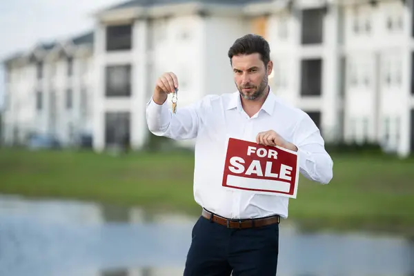Businessman buying and selling houses and real estate. real state agent giving new house key. Estate agent with customer. man real state agent holds up a for sale sign and keys to the apartment.
