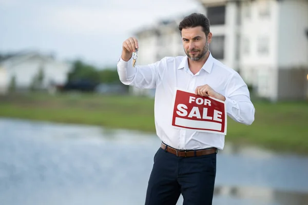 Businessman buying and selling houses and real estate. real state agent giving new house key. Estate agent with customer. man real state agent holds up a for sale sign and keys to the apartment.