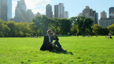  Yakışıklı iş adamı parkta dinleniyor. Şehir parkında iş adamı öğle yemeği molası veriyor. New York Central Park 'ta takım elbiseli Amerikalı bir işadamı çimlerin üzerinde oturup telefonla konuşuyor.