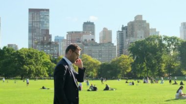  Yakışıklı iş adamı parkta dinleniyor. Şehir parkında iş adamı öğle yemeği molası veriyor. New York Central Park 'ta takım elbiseli Amerikalı bir işadamı çimlerin üzerinde oturup telefonla konuşuyor.