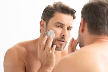 Adam banyoda nemlendirici yüz kremi kullanıyor. Krem tutan mutlu genç adam. Yüzüne krem süren 40 'lı yaşların portresi. Yakışıklı ciddi adam taze cilt kremi sürerek eğleniyor..