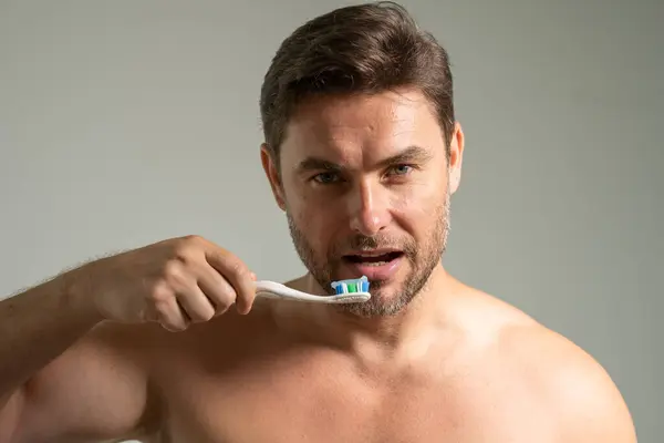 Man applying toothpaste on brush in bathroom, closeup. Attractive man looking down on toothpaste and brush. Taking care of teeth and mouth. Dental hygiene, vitality and beauty concepts