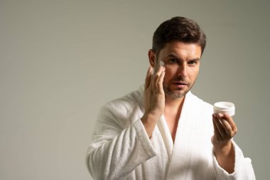 Genç, erkeksi bir adam yüz kremi sürüyor. Sağlıklı ciltli çekici bir adamın yakın çekimi, kırışıklık önleyici veya yaşlanmayı önleyici krem sürmesi, vücut bakımı. Güzellik portresi. Vücut pozitif. Deri