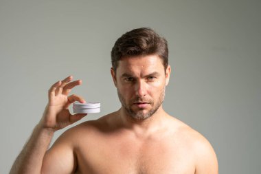 Genç, erkeksi bir adam yüz kremi sürüyor. Sağlıklı ciltli çekici bir adamın yakın çekimi, kırışıklık önleyici veya yaşlanmayı önleyici krem sürmesi, vücut bakımı. Güzellik portresi. Vücut pozitif. Deri