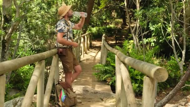 반바지와 셔츠를 관광객은 정글의 플라스틱 병에서 마신다 하이커 남자는 트레킹 — 비디오