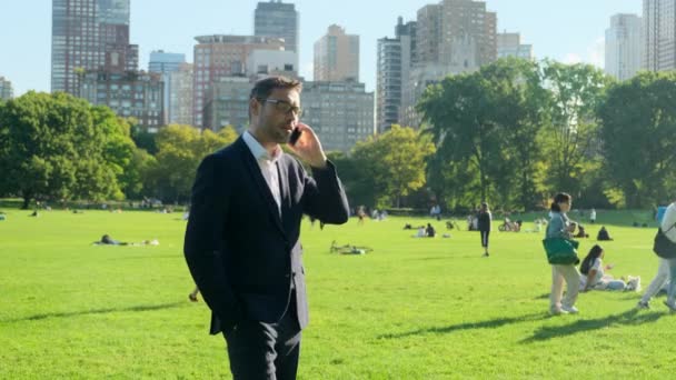 一位英俊的商人在公园里休息 市区公园的商人正在吃午饭 一位身穿纽约中央公园西装的美国商人坐在草地上 一边打电话一边聊天 — 图库视频影像