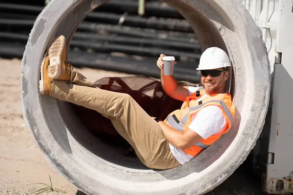 Coffee, engineer and construction worker relax on break at construction site. handsome male builder in hard hat smiling at camera. Construction Worker on Duty. Contractor and the Wooden House Frame
