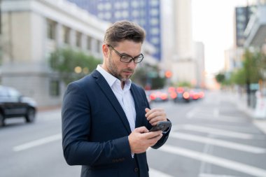 Yakışıklı genç bir işadamı telefonunu kullanıp sokakta dikiliyor. Yakışıklı, gülümseyen genç iş adamı şehrin dışında cep telefonu kullanarak şık bir şekilde dikiliyor.