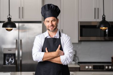 Gözlüklü, siyah şapkalı, parlak, modern bir mutfakta kolları çapraz duran kendine güvenen bir şef..