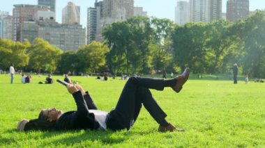 New York 'taki Central Park' ta takım elbiseli bir adam çimlerin üzerinde telefonuyla yatıyor. New York 'taki Central Park' ta çimlerin üzerinde uzanan bir işadamı bir mesaj yazıyor. Adam borsaya bakıyor.