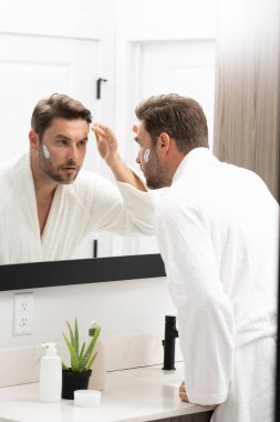 Bir adam aynanın önünde yüzüne losyon sürüyordu. Kişisel bakım ve kişisel bakım kavramı