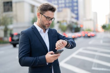 Yakışıklı genç bir işadamı telefonunu kullanıp sokakta dikiliyor. Yakışıklı, gülümseyen genç iş adamı şehrin dışında cep telefonu kullanarak şık bir şekilde dikiliyor.