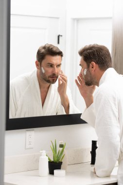 Bir adam aynanın önünde yüzüne losyon sürüyordu. Kişisel bakım ve kişisel bakım kavramı