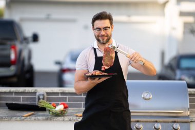 a man in an apron grilling a steak. Barbeque on holiday picnic. Man grilling a steak on BBQ. Grill and barbecue cook. Chef with BBQ cooking tools. Barbecue and grill. Picnic barbecue party. clipart