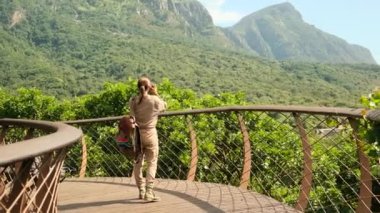 Güney Afrika, Cape Town 'da asma köprüde dağların fotoğrafını çeken bir kadın turist. Sırt çantalı gezgin yeşil ormanlarda dinleniyor ve eğleniyor. Turist kayalık orman yolunda seyahat ediyor.