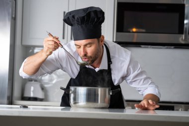 Profesyonel üniformalı modern şef. Kaşıkla tencereye çorba karıştıran erkek aşçının eline yakın plan. Yemek pişirme, aşçılık ve insan konsepti - erkek aşçı tencereli veya tencereli.
