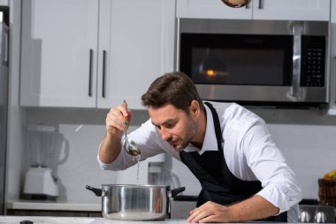 Profesyonel üniformalı modern şef. Kaşıkla tencereye çorba karıştıran erkek aşçının eline yakın plan. Yemek pişirme, aşçılık ve insan konsepti - erkek aşçı tencereli veya tencereli.
