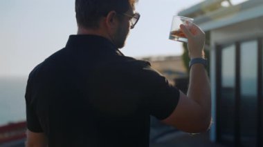 Terasta viski içen tişörtlü bir adam. Degukasyon, tatma. Sakallı adam elinde brendi bardağı tutuyor. Tatma ve degukasyon konsepti. Zarif takım elbiseli sakallı bir işadamı ve bir bardak viski.